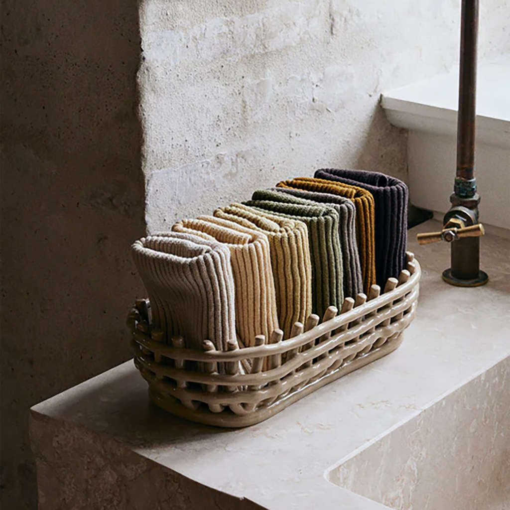 Ferm Living Ceramic Basket Oval in Cashmere, woven-look ceramic catch-all with folded towels on a stone countertop