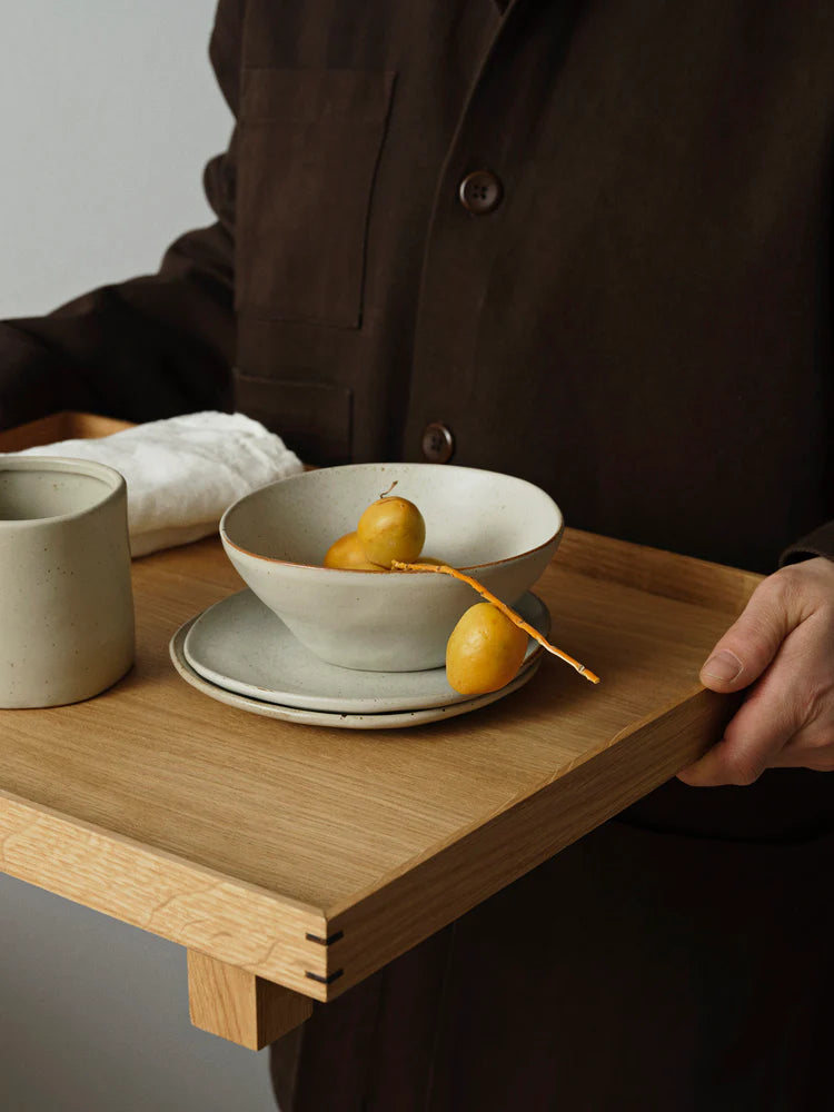 Ferm Living Flow tableware in Off-White Speckle — porcelain plate and bowl with semi-matte glaze styled on wooden tray with mug and fresh fruit.