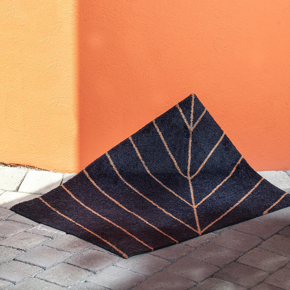 Eine Nightfall black doormat with golden geometric lines, shown in natural light.