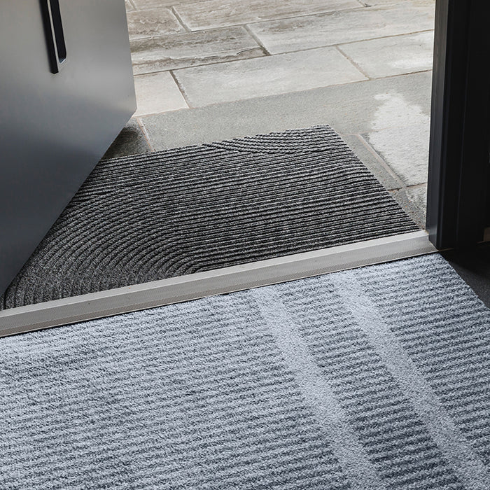 Heymat Loype Stormy Blue doormat with ski-track inspired pattern, recycled PET surface, non-slip rubber backing, styled in modern entryway