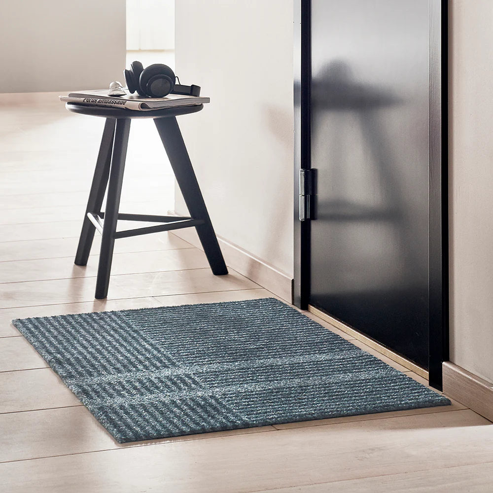 Heymat Loype doormat in Stormy Blue on a white oak floors in front of a black door with Scandinavian side table.