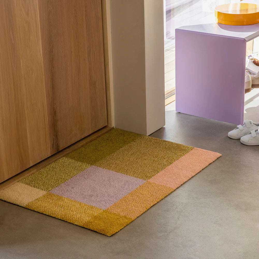 Mix Teklan color-blocked doormat, styled in modern entry with lavender side table and concrete floors.