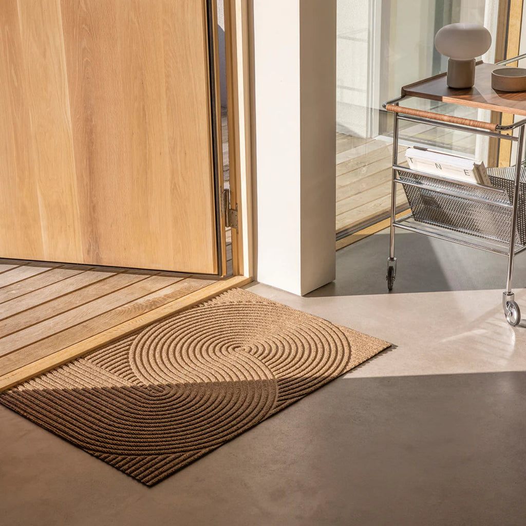 Heymat Sand doormat with Zen garden-inspired 3D ripple pattern, styled in modern Scandinavian entryway with cement floors