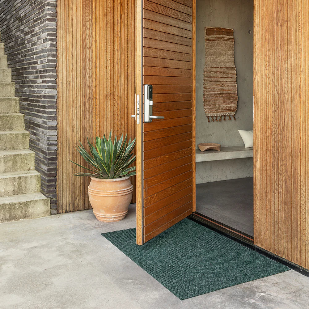Heymat Stra doormat with minimalist stripe pattern, styled in bright modern entryway with cement floors and wood accents.