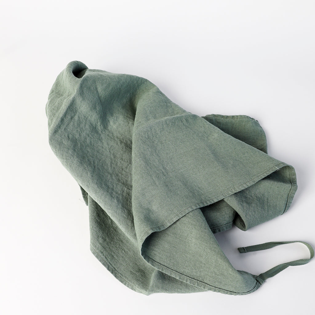 Linge Particulier linen dish towel in soft sage green washed linen, shown loosely folded to highlight its natural texture and cotton hanging tie.