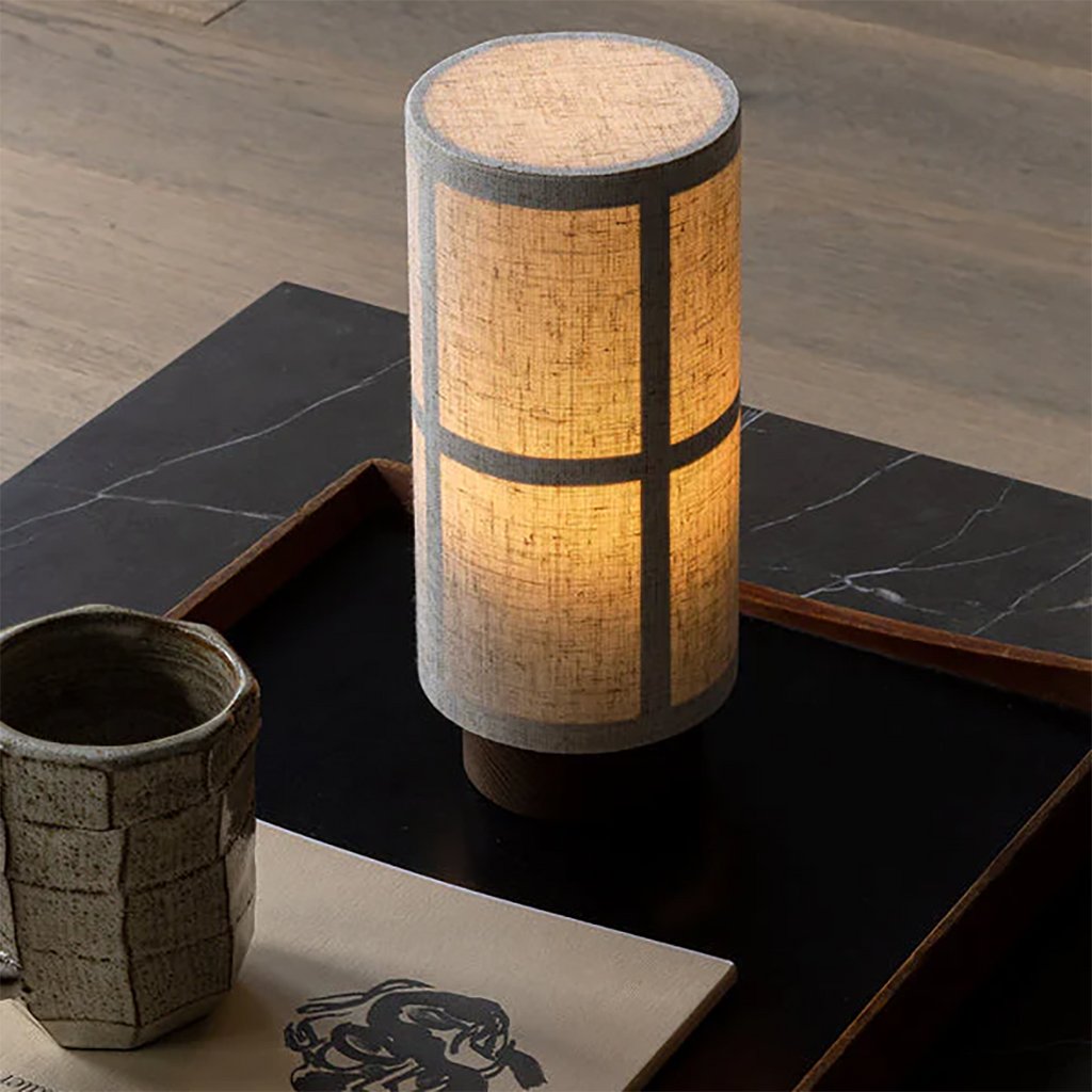 Audo Copenhagen Hashira Portable Lamp casting a warm glow on a side table in a softly lit modern interior.