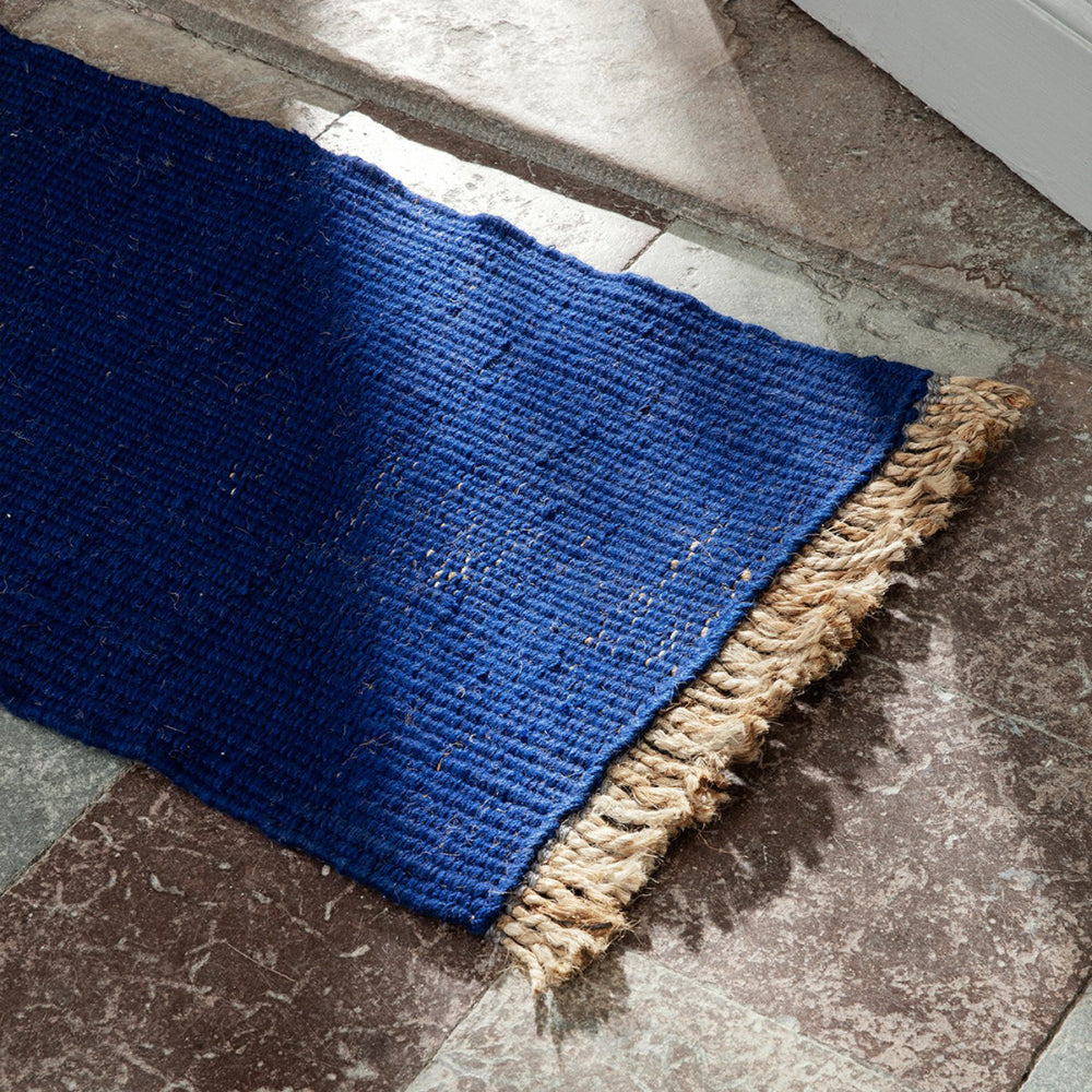 Bright Blue Block Mat with natural fringe on stone floor under natural light showing woven texture.
