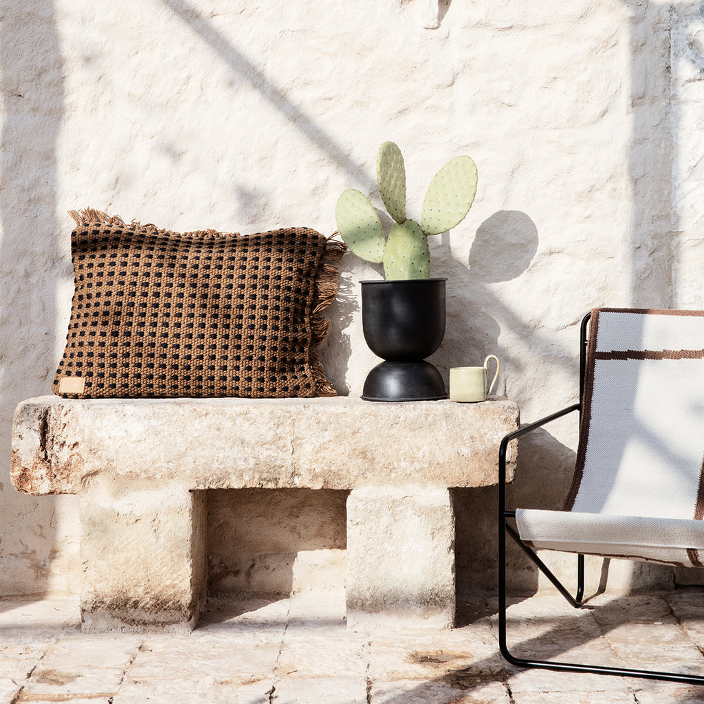 Hourglass Pot XS in black styled outdoors with minimalist décor and succulant plant cascading over the rim.