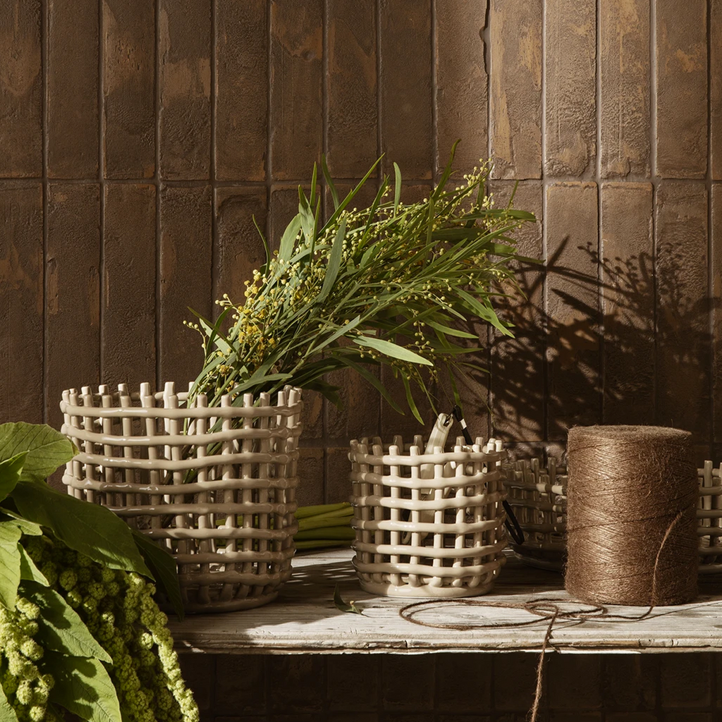Ferm Living Ceramic Basket Large in Cashmere — handcrafted glazed ceramic baskets styled on a rustic worktable with greenery and twine, set against a warm brown tiled wall