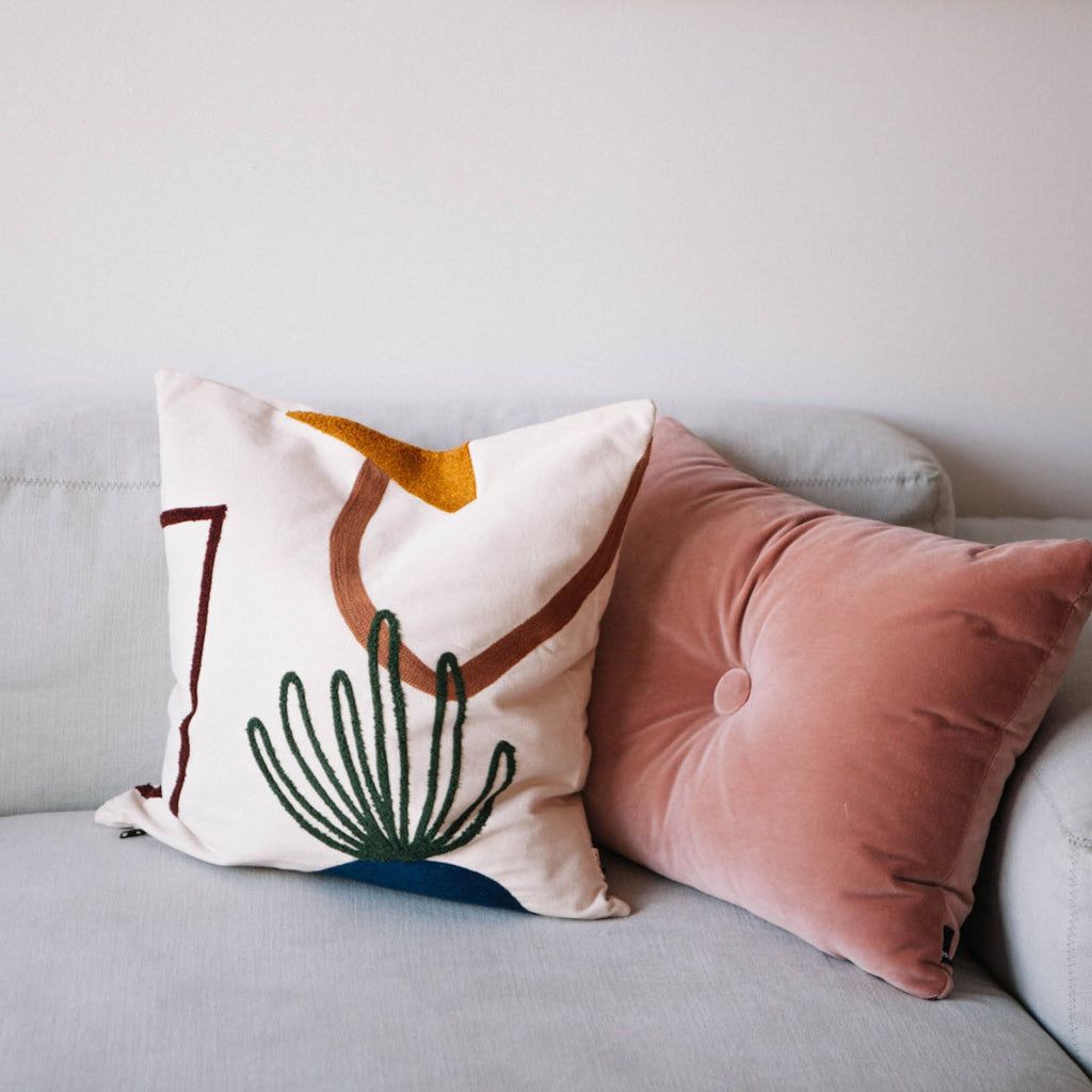 Mirage Cushion in Island styled on a neutral sofa beside pink velvet cushion on light grey, modern sofa adding warmth and texture.