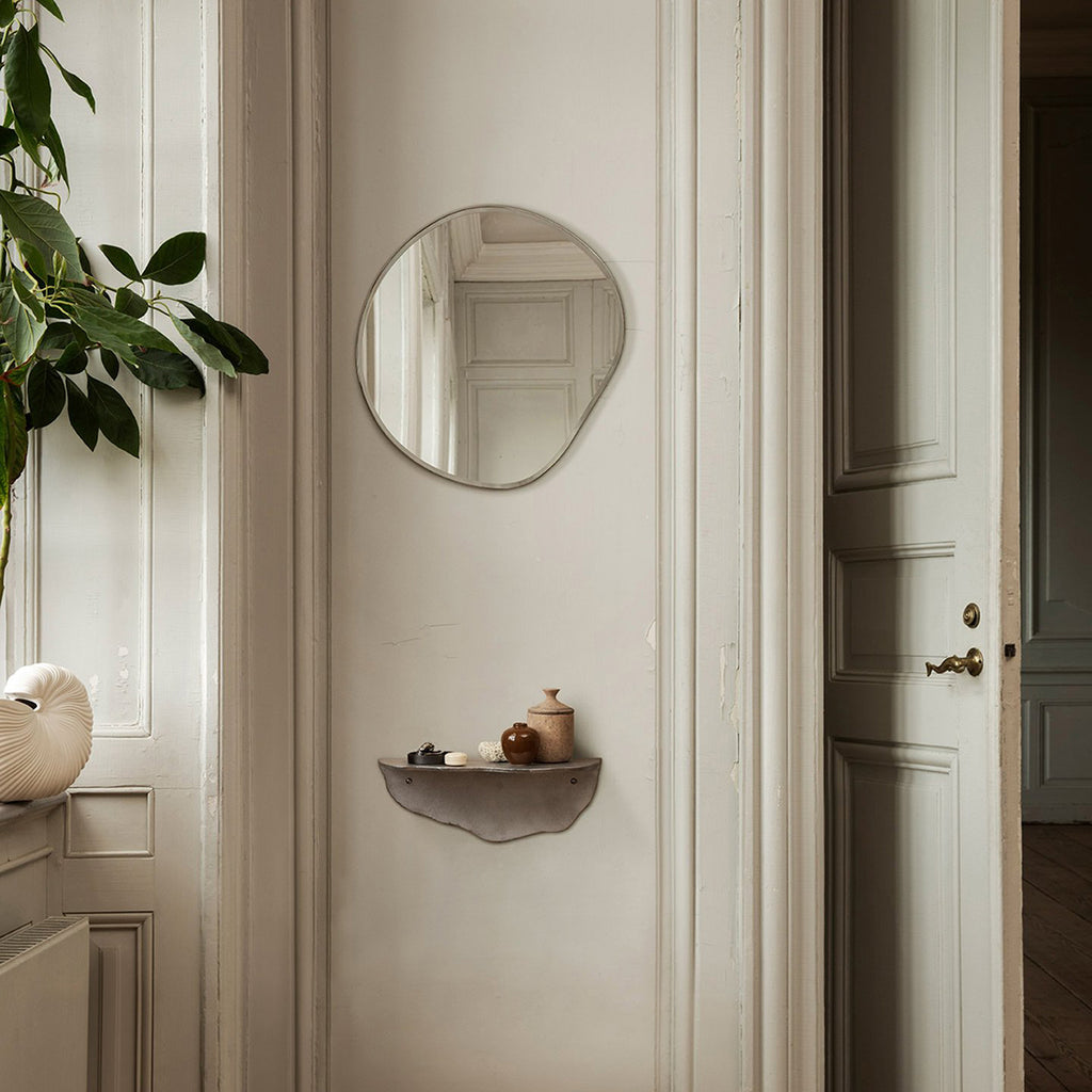 Ferm Living Pond Mirror Small in dark chrome styled in a classic entryway with sculptural ceramics and greenery, reflecting soft natural light against neutral paneled walls.