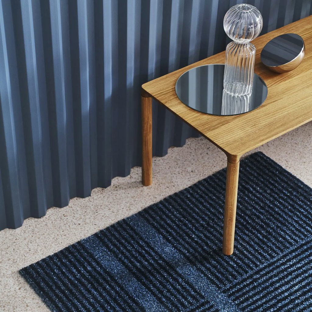Heymat Løype Cloudy Grey mat, washable and slip-resistant, modern entryway rug styled in modern entryway on terrazzo floor with natural wood table