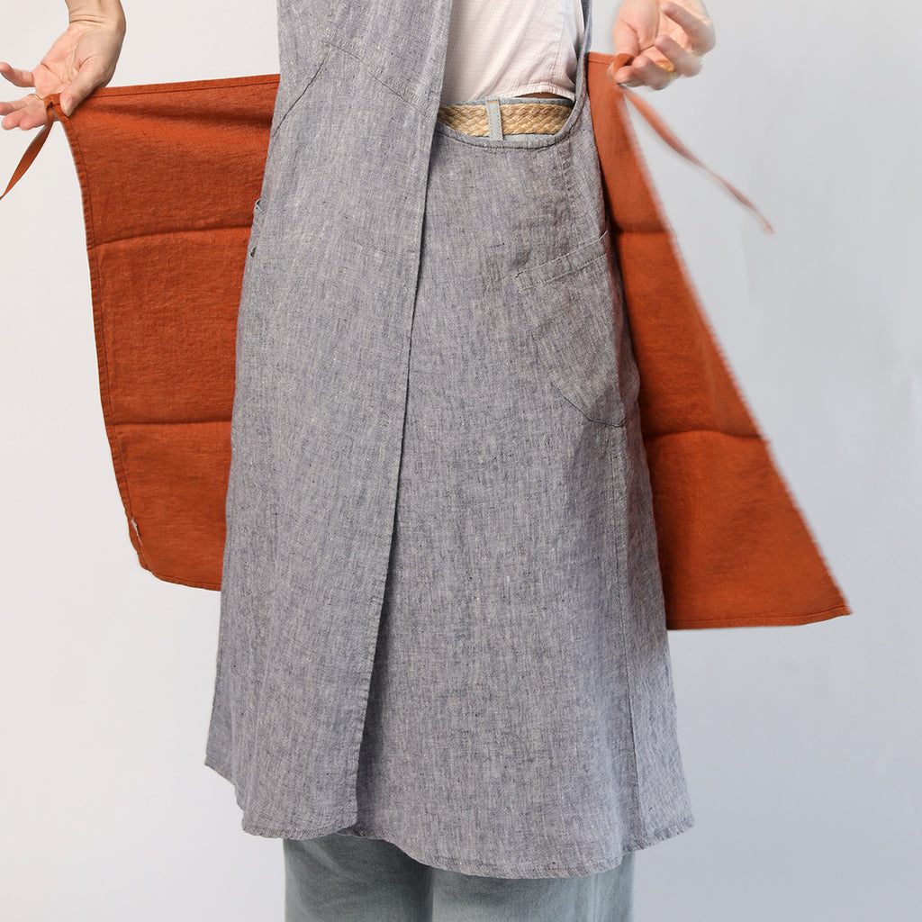 Linge Particulier linen dish towel in terracotta shown tied around the waist as an impromptu apron, highlighting its soft washed texture and versatile cotton ties.