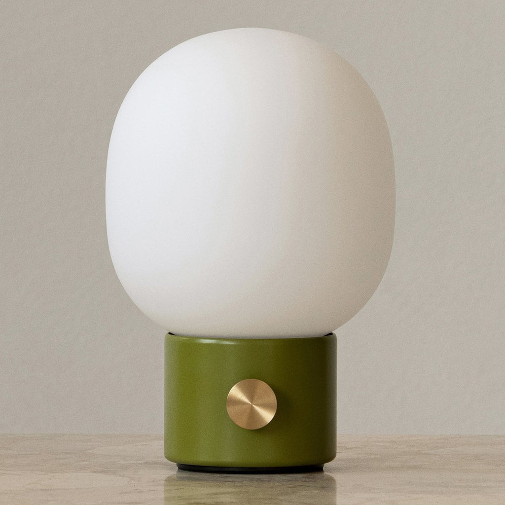 Audo Copenhagen JWDA Portable Lamp in dusty green with frosted glass shade and brass dimmer, shown on a marble table with neutral background.