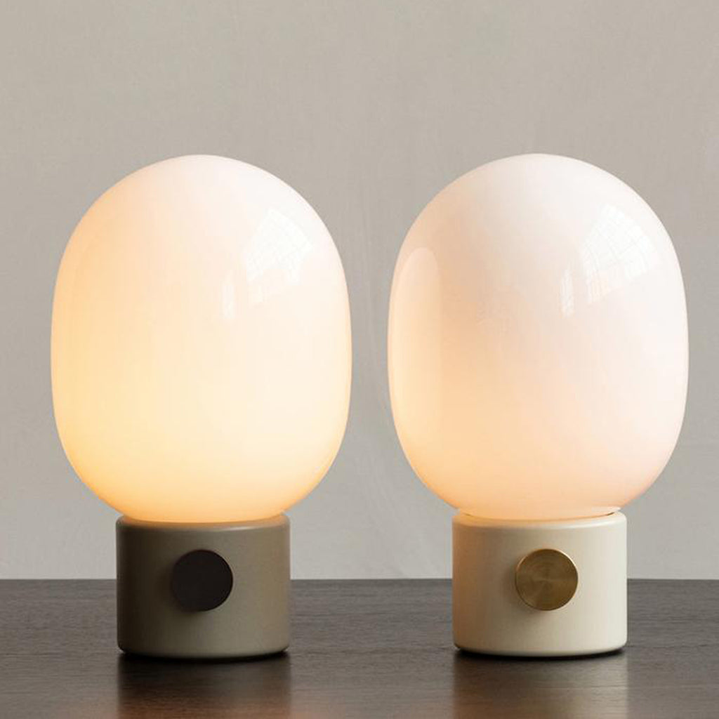 Audo Copenhagen JWDA Portable Lamps in Dusty Green and Alabaster White with frosted glass shades and metal dimmer knobs, shown illuminated on a neutral surface.