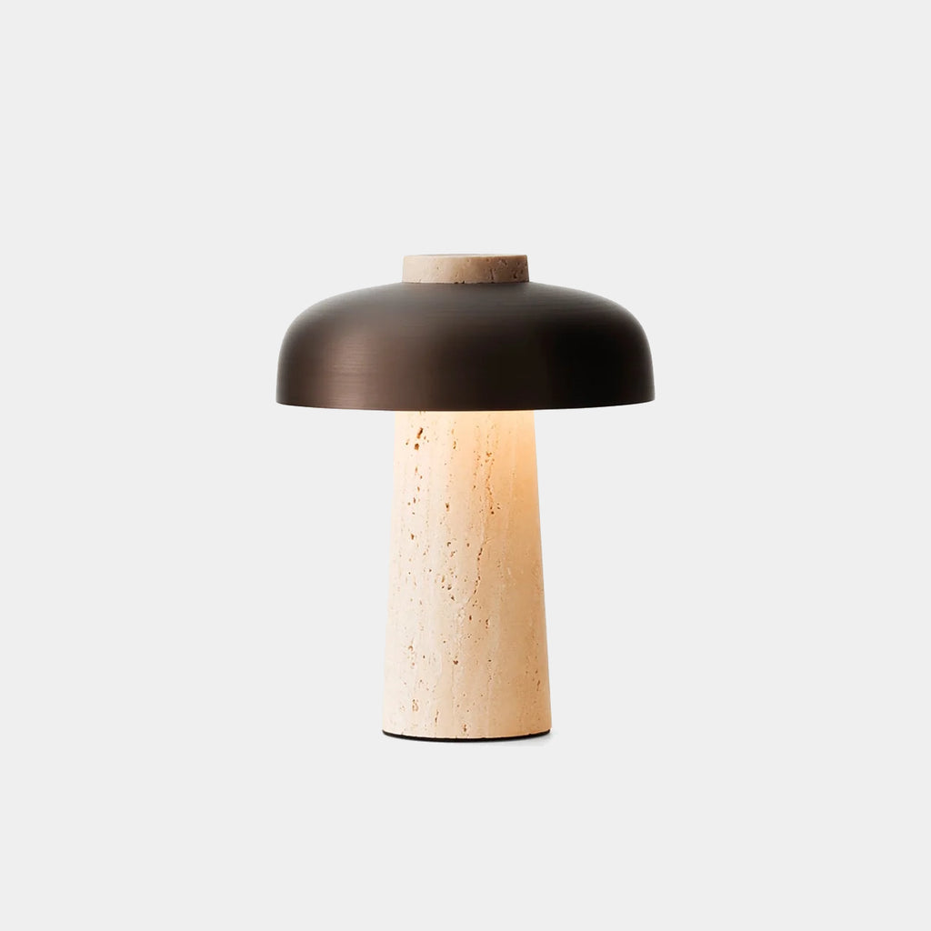 Reverse Portable Table Lamp with conical travertine base and curved bronzed metal shade on neutral background shown with light on