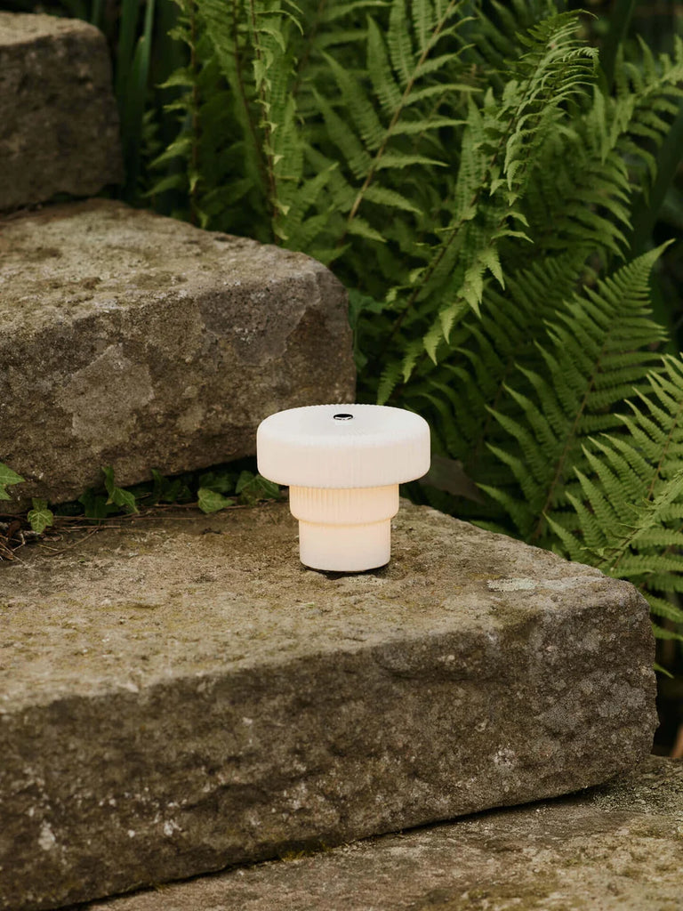 Ferm Living Ripple Portable Lamp in White styled outdoors among stone and ferns