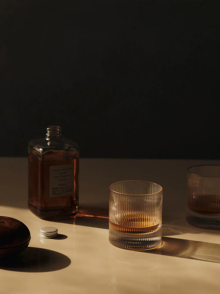 Ferm Living Ripple Tumbler in Frosted Glass with whiskey bottle on neutral surface in soft light