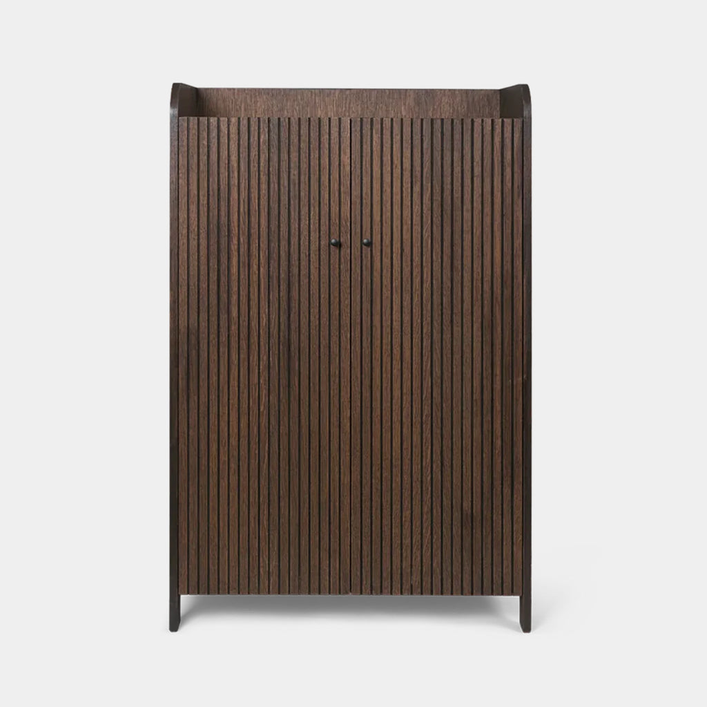 Front view of the dark oak Ferm Living Sill Cupboard in dark stained oak with vertical fluted doors and black knobs
