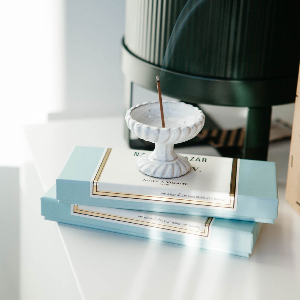 Astier de Villatte Peggy incense holder in milky-white glazed ceramic, shown with incense and green plant pot.