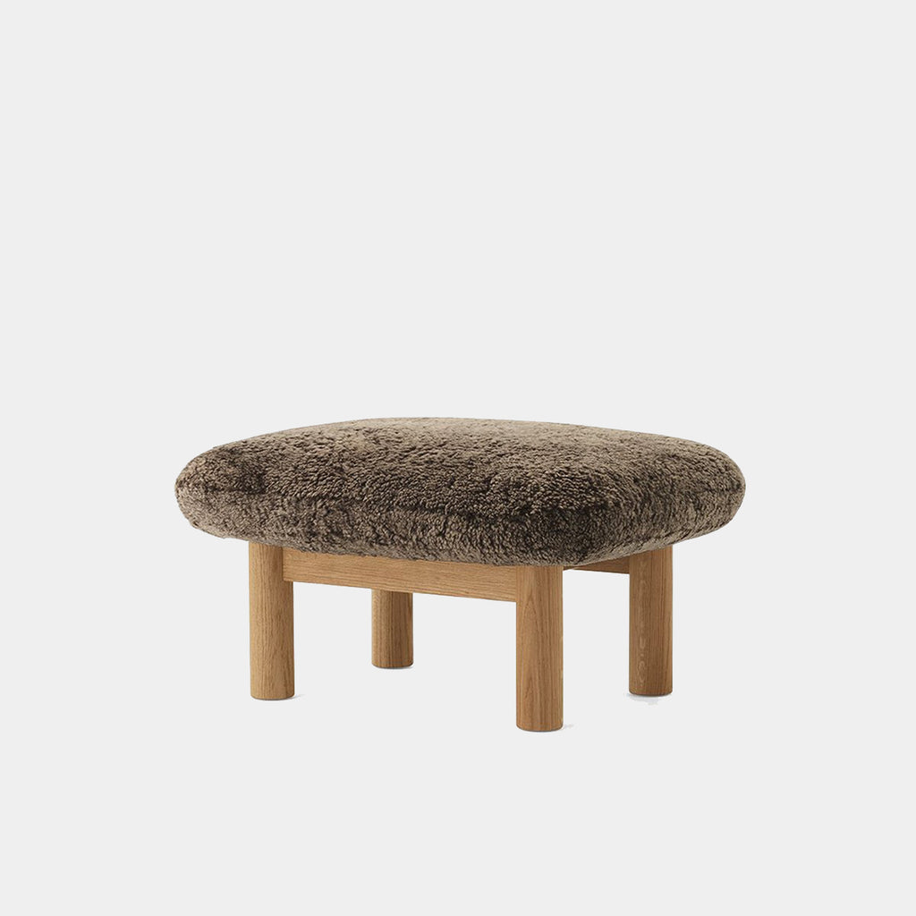 Audo Copenhagen Brasilia Ottoman in walnut with Sheepskin Root upholstery, highlighting its warm tone and tactile texture against a neutral background.