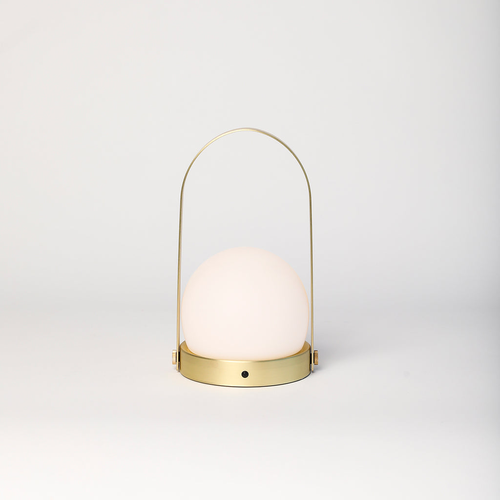 Audo Copenhagen Portable Carrie LED Lamp in brushed brass with opal glass shade on neutral background