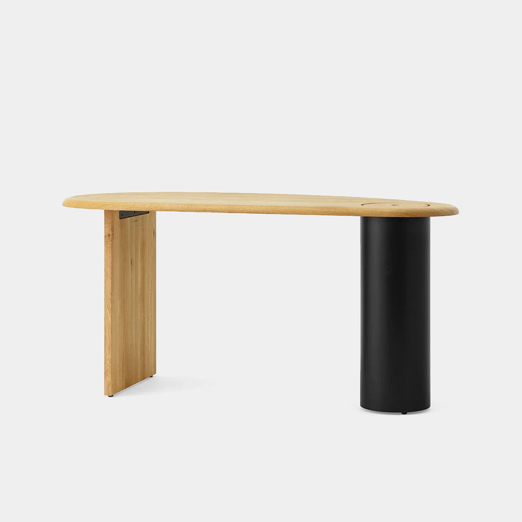 Audo Copenhagen Eclipse Desk in natural oak with sculptural curved tabletop and black steel leg, shown on a neutral background.